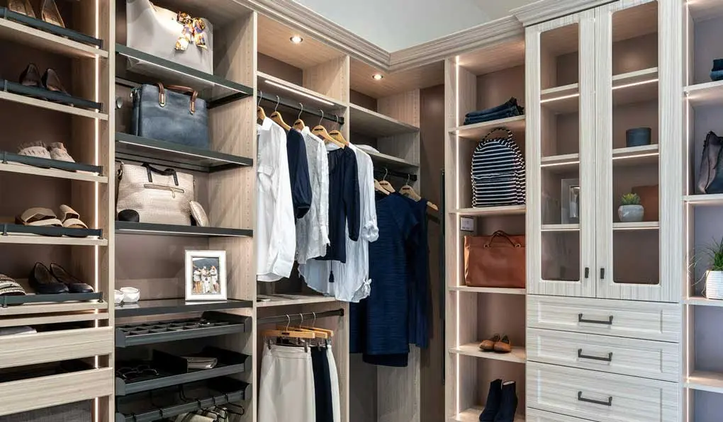 light beige wood closet with lighting system glass shelves and dark hardware