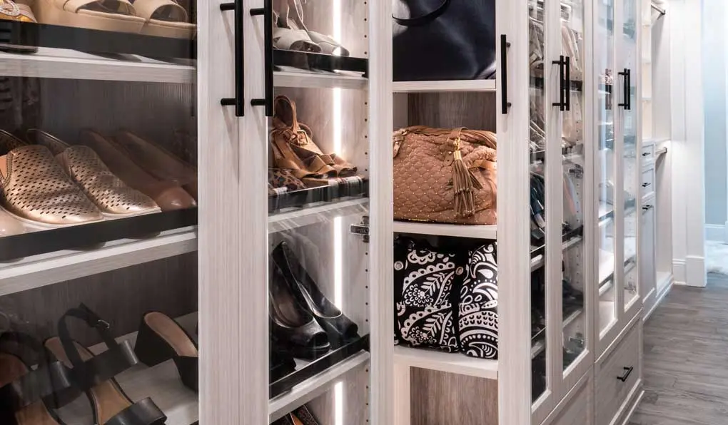 shoes and bags neatly organized inside custom closet with glass door and white shelves with black hardware