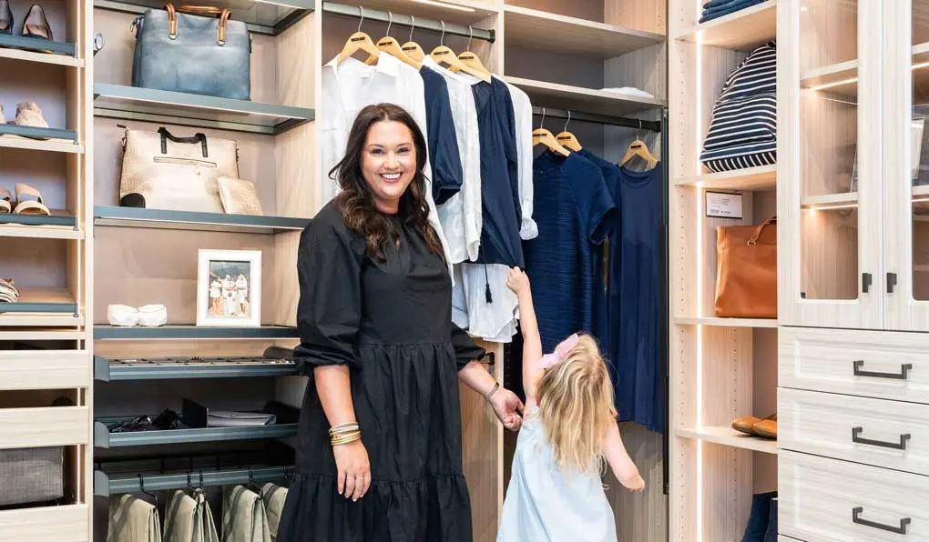 A woman smiling at the camera and a child pulling on clothes hanging in a light beige wood custom shelving